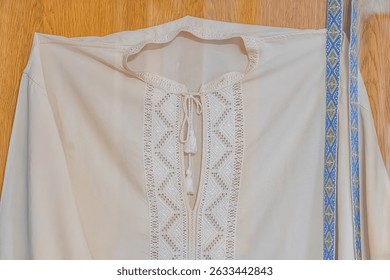 Embroidered fabric piece on wooden surface, traditional design, floral or paisley motifs, symmetrical geometric patterns, dense embroidery, creamlight yellow background, decorative borders, blue con