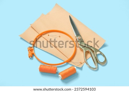 Embroidery hoop with canvases, scissors and thread spools on blue background