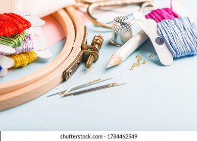 Embroidery set fot cross stitching. White fabric, embroidery hoop, colorful threads, scissors and needls. On blue background. Hobbies concept with copy space.