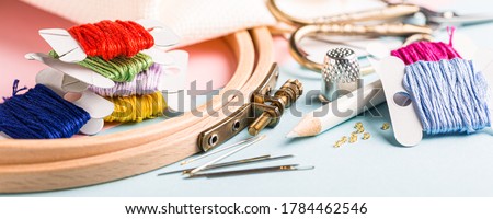 Embroidery set fot cross stitching. White fabric, embroidery hoop, colorful threads, scissors and needls. On blue background. Hobbies concept. Banner