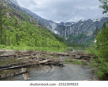 Emerald forests hug towering cliffs, while misty waterfalls tumble into a serene lake. The scent of pine and rain fills the crisp air, as rippling water whispers softly over driftwood and stone.