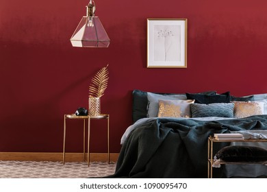 Emerald Green Bed Against Red Wall With Poster In Bedroom Interior With Lamp Above Gold Table