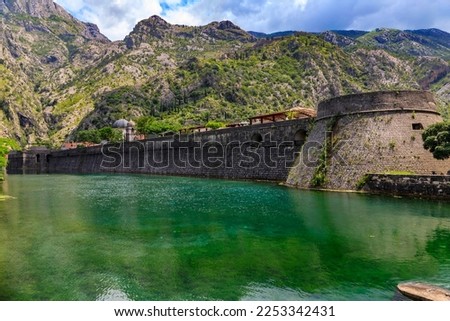 Emerald green waters of Kotor Bay or Boka Kotorska, mountains and the ancient stone city wall of Kotor old town former Venetian fortress in Montenegro