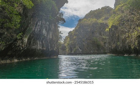 The emerald Lagoon is surrounded by inaccessible sheer karst cliffs. Green vegetation on steep furrowed slopes. The canoe is far away. Blue sky, clouds. Philippines. Palawan. Small Lagoon. Bacuit Bay - Powered by Shutterstock