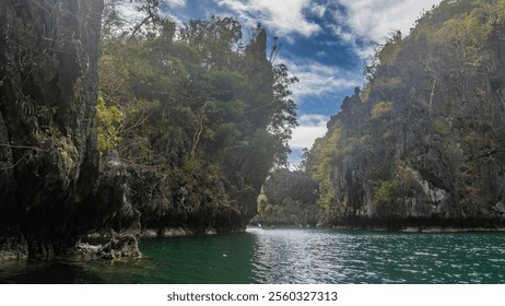 The emerald Lagoon is surrounded by sheer cliffs. Green tropical vegetation on steep slopes. Ripples on calm water. Blue sky, clouds. Philippines. Palawan. Small Lagoon. Bacuit Bay. - Powered by Shutterstock