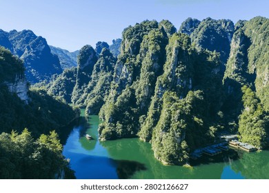 Emerald river meanders through dramatic karst limestone formations covered in lush green vegetation in this stunning natural landscape.