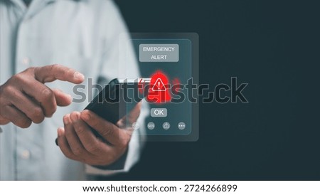 Emergency alert concept. Hand using smartphone with warning notification and alert icon on screen. Crisis notification, emergency response, risk management, mobile technology, public safety system.