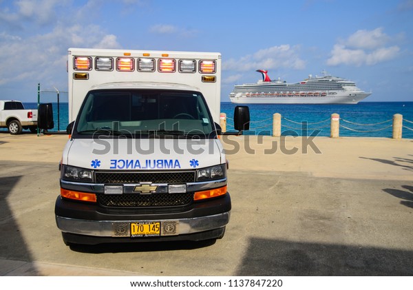 Emergency ambulance\
at port of Grand Cayman island and a ship of Carnival cuise lines\
at the back. July 8,\
2018