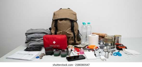 Emergency backpack equipment organized on the table. Documents, water,food, first aid kit and another items needed to survive. - Shutterstock ID 2180383547