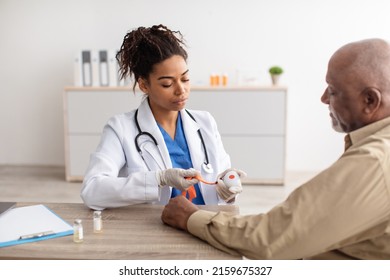 Emergency Button Concept. Portrait Of Black Medical Worker Holding Personal Alarm Button And Giving It To Senior Patient, Sitting At Table In Office. Older Male Looking At Medical Alert