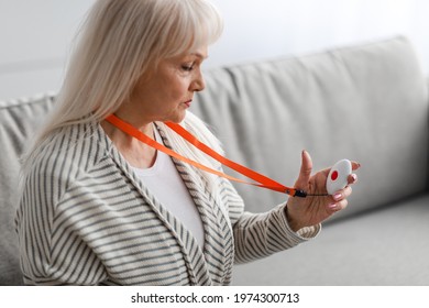 Emergency Button Concept. Portrait of serious senior lady holding personal alarm button, sitting on the at home alone. Older female looking at medical alert, selective focus