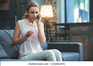 Emergency Call. Concerned Mature Woman Carrying Glass Of Water And Talking On Phone