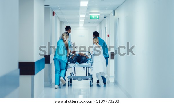 Emergency Department: Doctors, Nurses and\
Paramedics Push Gurney / Stretcher with Seriously Injured Patient\
towards the Operating Room. Bright Modern Hospital with\
Professional Staff Saving\
Lives.