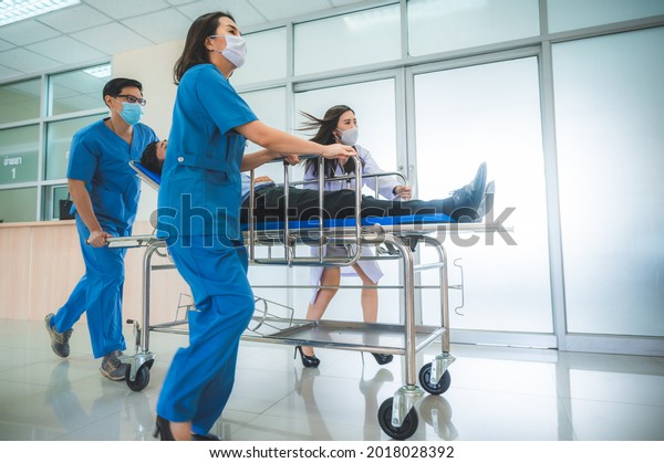Emergency\
Department: Doctors, Nurses and Paramedics Run and Push Gurney \
Stretcher with Seriously Injured Patient towards the Operating\
Room. Modern Hospital with Professional\
Staff.
