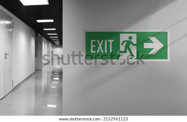 Emergency exit sign. Interior internal corridor of\
modern office. Corridor with light walls, black ceiling and shiny\
floor. Soft focus.