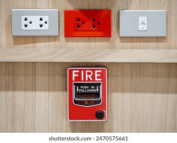 Emergency fire warning system pull station. Red fire alarm mounted on wooden wall near electrical power socket and telephone socket in public building