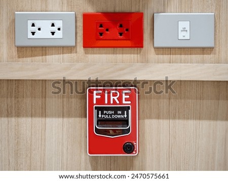 Emergency fire warning system pull station. Red fire alarm mounted on wooden wall near electrical power socket and telephone socket in public building