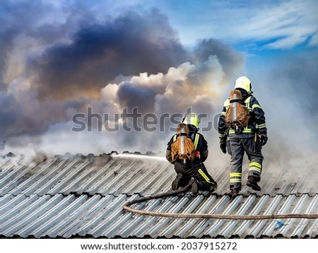 Emergency. Firefighters extinguish the flame on the roof of the building. Roofing houses covered fire. Rescuers pour fire. Firefighters in uniform. Fire on the roof of the house.