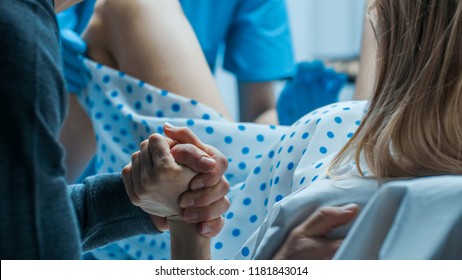 Emergency In the Hospital: Woman Giving Birth, Husband Holds Her Hand in Support, Obstetricians Assisting. Modern Delivery Ward with Professional Midwives.