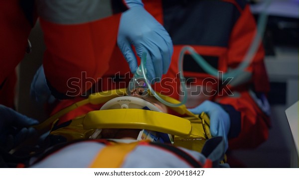 Emergency medical doctors providing medical help for\
patient in oxygen mask. Health care professionals rescuing victim\
of drill car crash. EMS paramedics fixing man head on stretchers in\
ambulance car