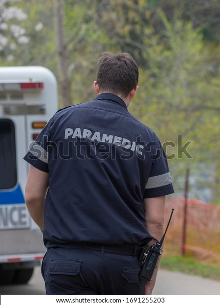 Emergency medical service worker with\
paramedic sign on the uniform walking towards the EMS truck.\
Selective focus, blurred\
background.