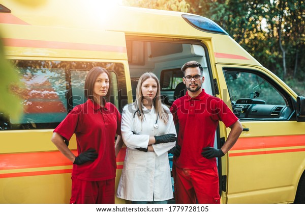 Emergency medical service workers man\
and woman standing and posing in front of ambulance\
car.