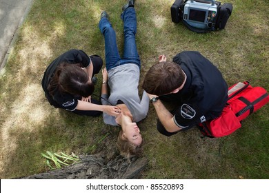 Emergency medical team responding to a woman in a park - Powered by Shutterstock