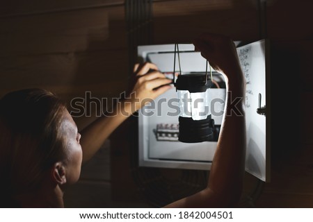 emergency power outage in house. woman with flashlight looks into distribution board. Short circuit.
