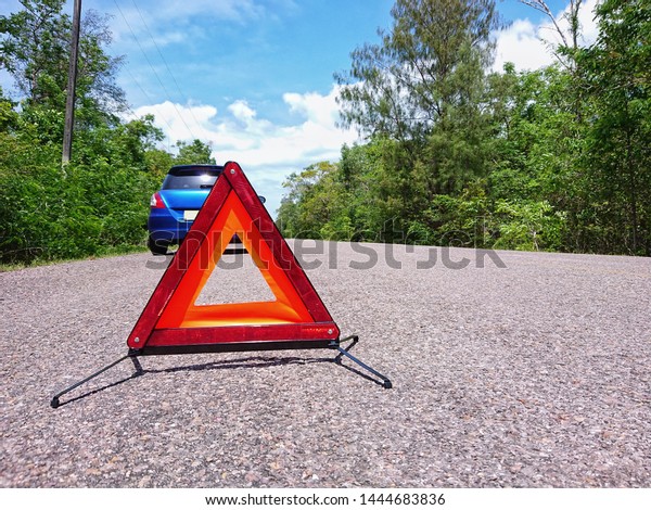 Emergency red warning triangle on the road sign with\
a blue broken car