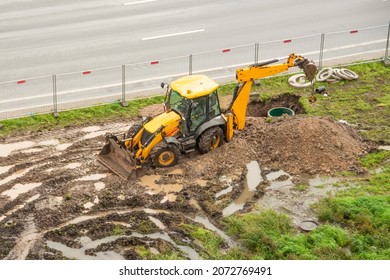 Emergency Repair Work Of Main Urban Heat Pipes On The Lawn Nearby. Working Tractor Excavator Digs A Pit Trench At Site Of Heating Failure