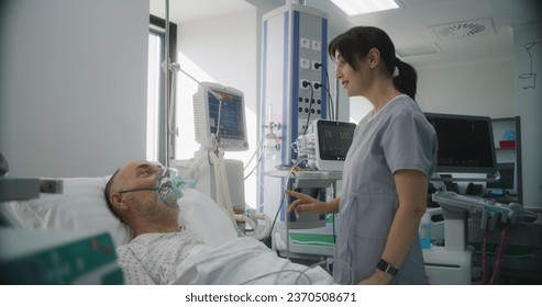 Emergency room with modern equipment in clinic. Senior man in oxygen mask lies in bed during lung ventilation. Friendly nurse adjusts life support machine for old patient. Intensive care department. - Powered by Shutterstock