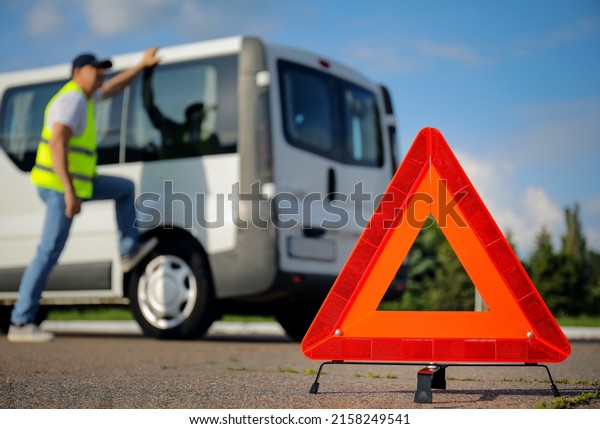 Emergency triangle stop sign and man near broken car\
on road