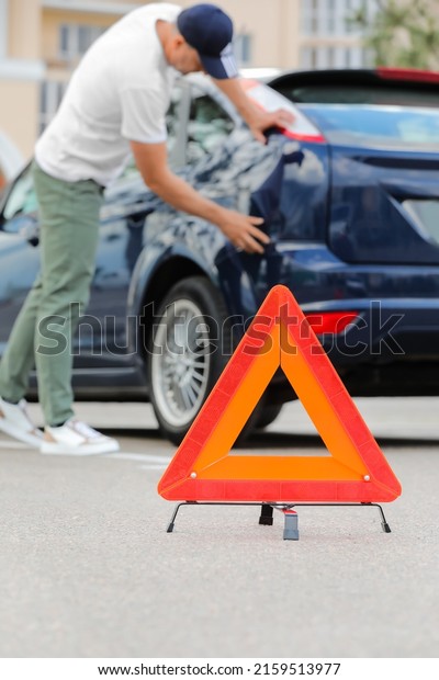 Emergency triangle stop sign and man near broken\
car outdoors