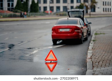 Emergency warning triangle placed behind vehicle after minor rear end collision on wet city road during evening traffic, road safety precautions and hazard signaling for approaching motorists