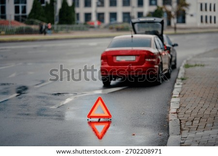 Emergency warning triangle placed behind vehicle after minor rear end collision on wet city road during evening traffic, road safety precautions and hazard signaling for approaching motorists