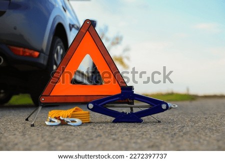 Emergency warning triangle, towing strap and scissor jack near car outdoors. Safety equipment
