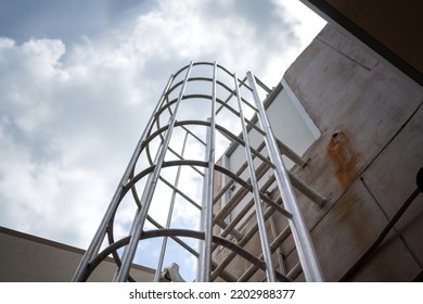 An Emergency Way Climbing Ladder With Falling Prevetion Cage At The Outside Of Factory Building. Industrail Equipment Object Photo, Selective Focus At Some Rail Step.