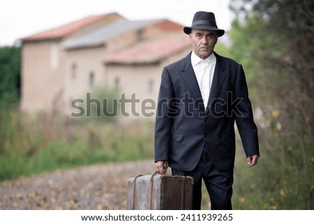 emigrant with suitcase and vintage suit leaving his village to look for work at early 20th century , caucasian man on old photography