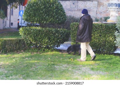 EMILIA ROMAGNA, ITALY - Dec 23, 2021: A Senior Caucasian Man Having A Walk In The Garden With His Black Terrier Dog