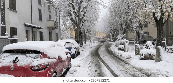TOLÉ, EMILIA ROMAGNA, ITT – November 22, 2025: A narrow street lined with snow-dusted parked cars and bare trees under soft winter light in a rural village.