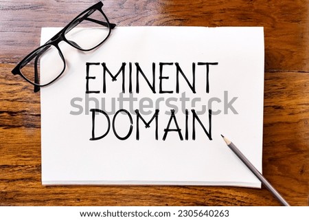 Eminent domain handwriting text on blank notebook paper on wooden table with pencil and glasses aside. Business concept and legal concept about eminent domain.