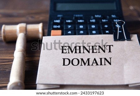EMINENT DOMAIN - words on light brown paper against the background of a calculator and a judge's gavel