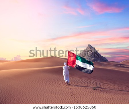 Emirati man holding UAE flag walking in the desert celebrate the national day - spirit of the union 