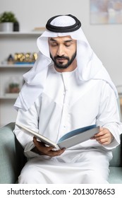 An emirati man wearing white kandura (Traditional cloth) reading a book