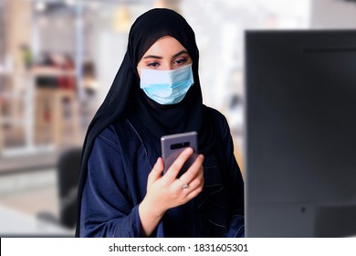 Emirati Office Girl Wearing A Face Mask While At Work. Arab Employee Checks Her Mobile Smartphone