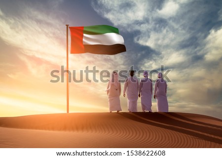 Emirati Young men standing on sand dune on the desert looking in  UAE flag celebrating national day and Uae flag day