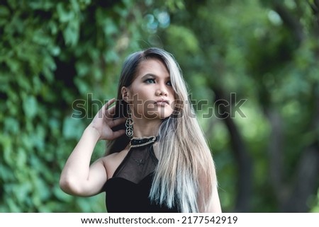 An emo and goth asian lady with blonde dyed hair in a black dress. Outdoor shoot.