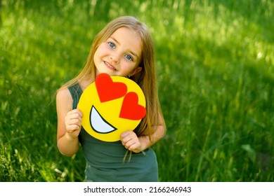 emoticon with hearts in the hands of a child. A beautiful smiling Girl defiantly shows a carton smile love face.