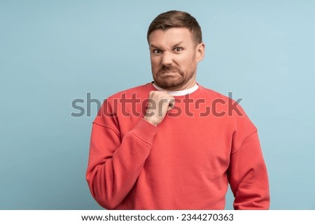 Emotion of disgust on face of young man. Middle aged male in red sweatshirt on blue background with bright expressive facial expressions looks at camera contemptuously with hostility, loathing.
