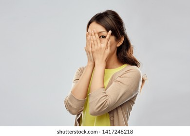 emotion, expression and people concept - scared asian woman peeking over grey background